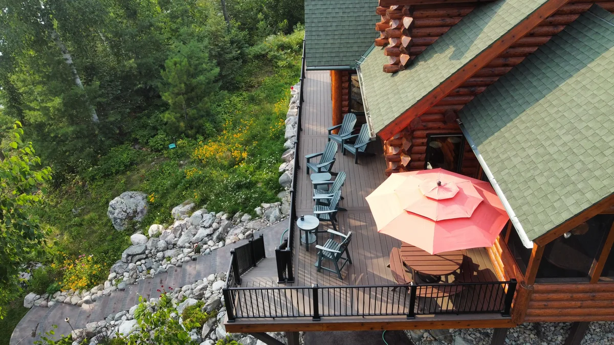 Westbury Tuscany railing around a log cabin deck with Adirondack chairs and a coral umbrella